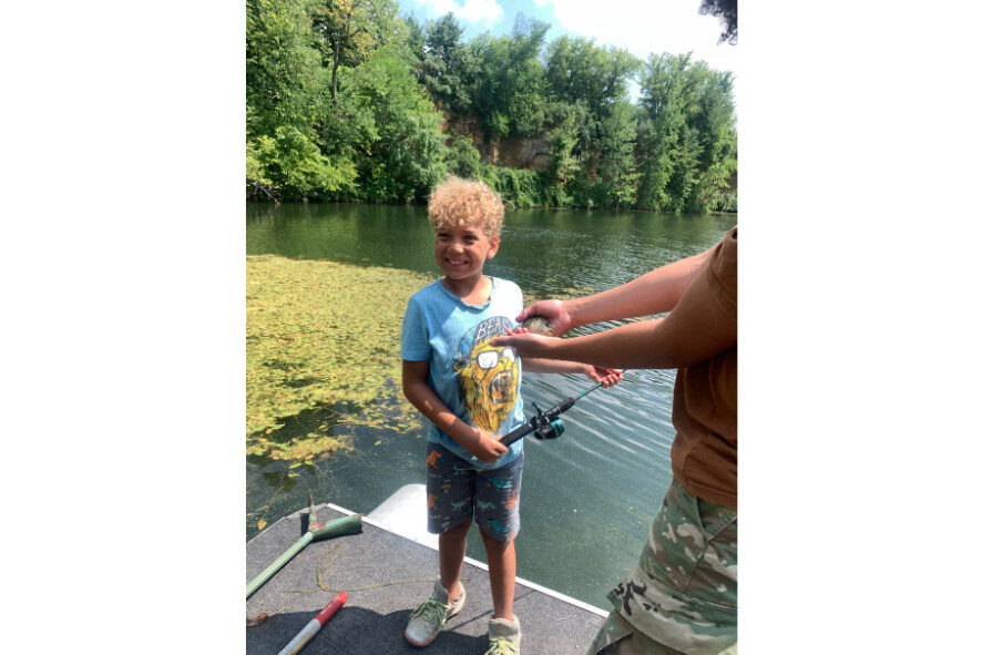 young person after catching his first fish standing next to the fish that someone else is holding