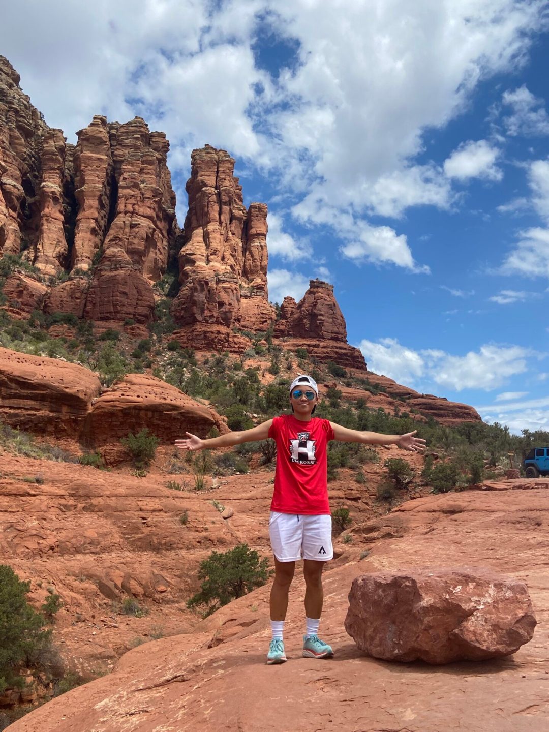 person standing on red rocks while on a hike with tall rock formations in the background