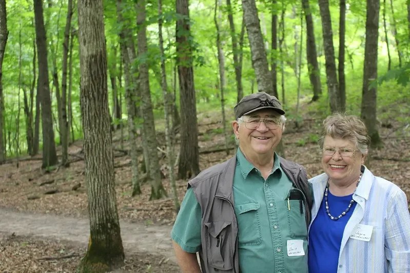two people standing in front of a paved trail in a forest