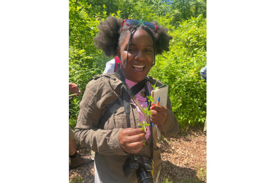 person smiling holding a plant and a notepad