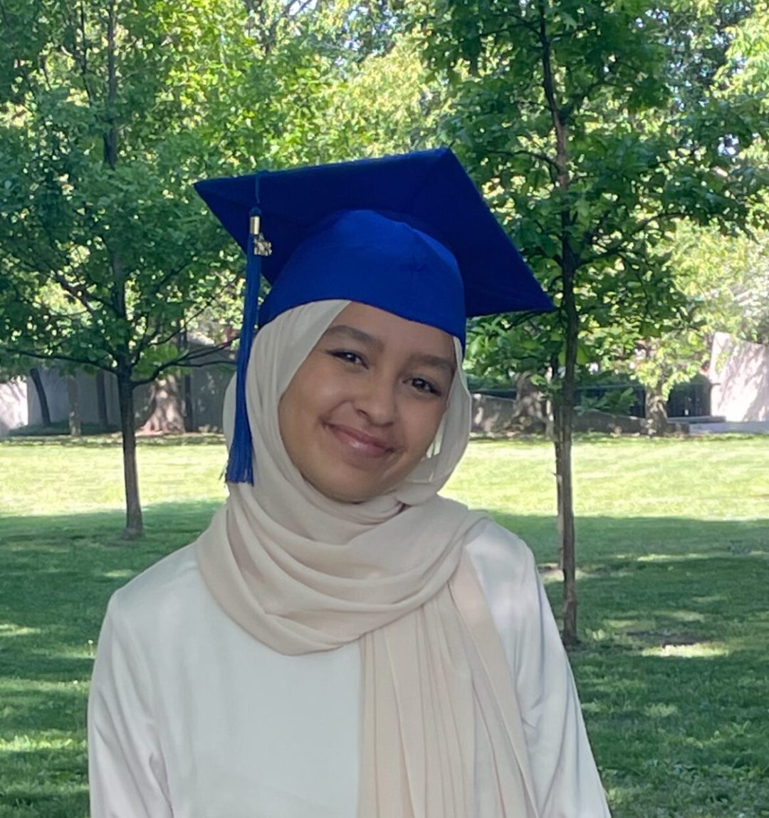 person smiling while wearing a graduation cap in a park