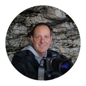 person taking a selfie while sitting in a cave and holding a DSLR camera