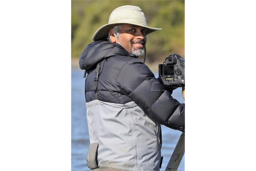 Sunil Gopalan standing next to his camera that is on a tripod 